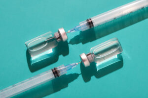 injectable vials and syringes on teal with trendy lighting and hard shadows