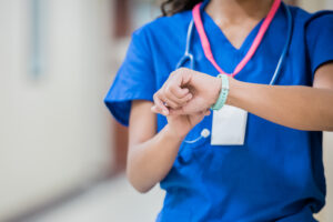 Young adult woman checks her smart watch or activity tracker during shift as a nurse in hospital emergency room.