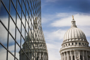 Horizontal view of the Wisconsin State Capitol Dome reflecting into the windows of a steel and glass office building on a sunny day.