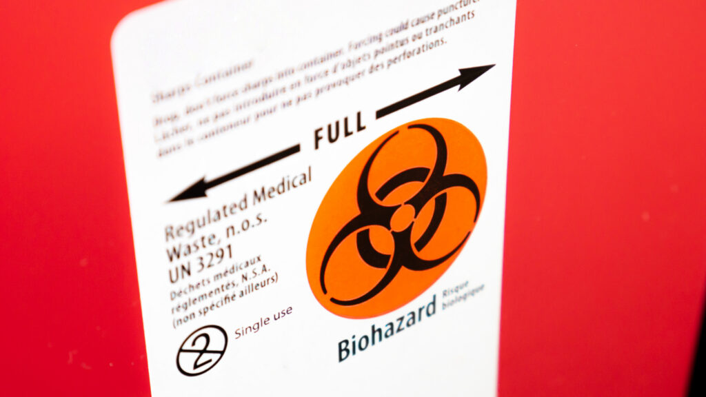 A sharps container for biohazardous waste, bearing the international symbol for biohazards and a bilingual description in English and French.