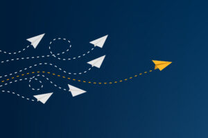 Yellow paper airplane leading white ones on a dark blue background. Represents leadership, innovation, and standing out.